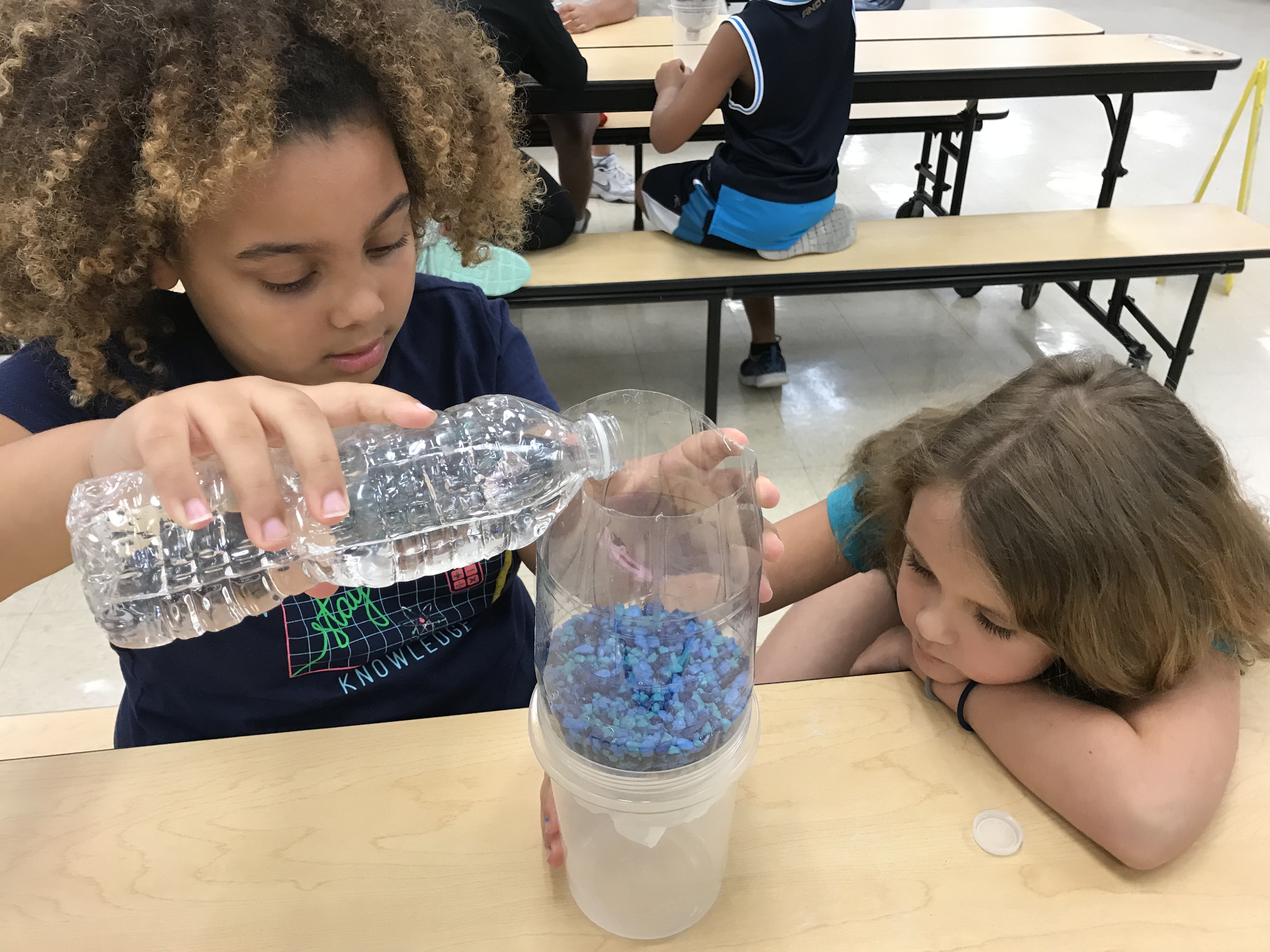 Girl pouring water into her water filter project as her partner watches