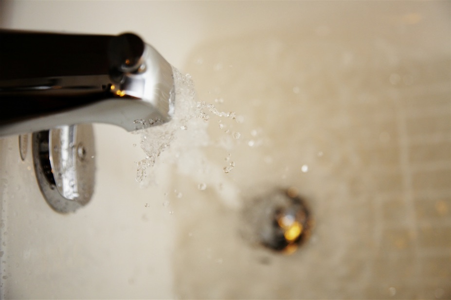 Water flowing from bathtub faucet into stoppered tub.