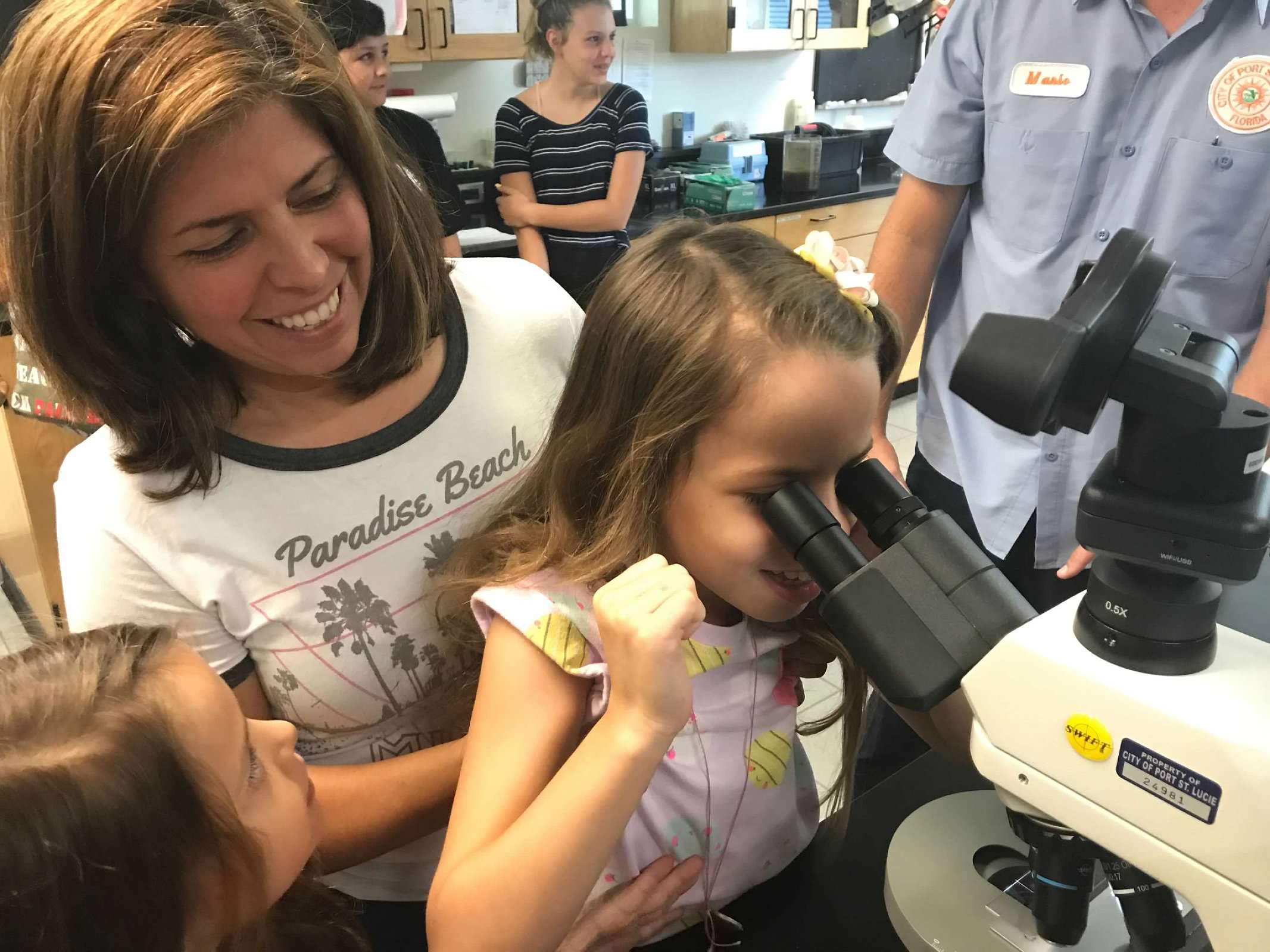 Mom holds her daughter up to microscope to see the microorganisms from the wastewater treatment plant