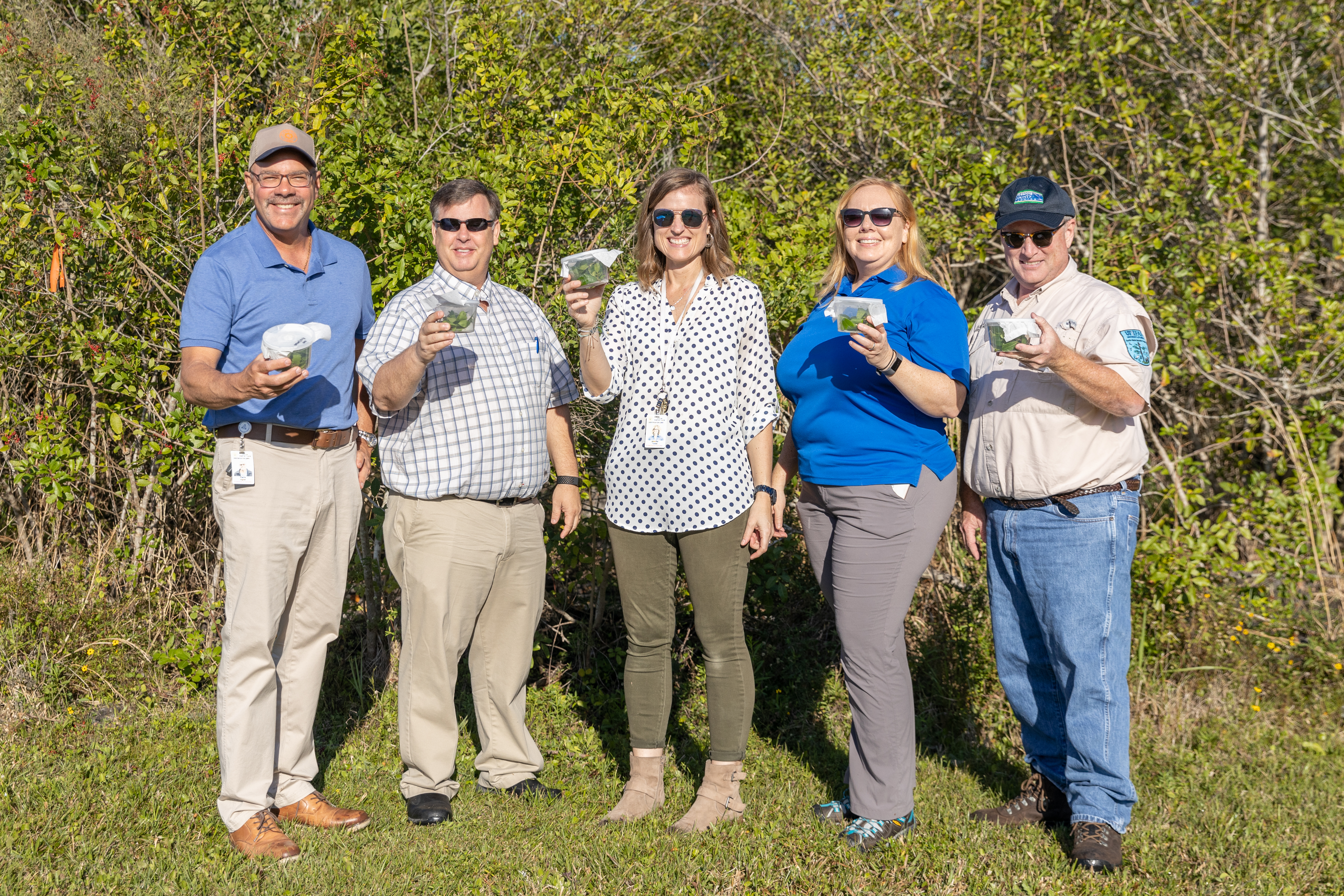 Utility Systems employees and IFAS Extension Agents hold up cups filled with thrips.